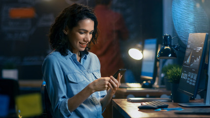 Wall Mural - beautiful female financier uses mobile phone, writing messages, emails while smiling. in the backgro