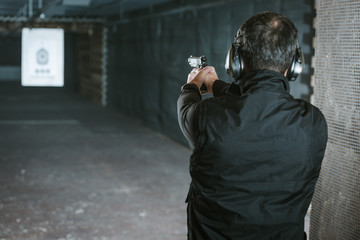 rear view of man aiming gun at target in shooting range