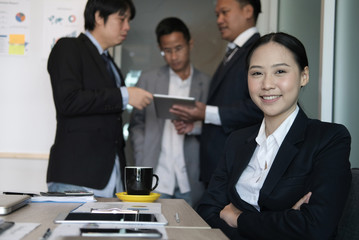 asian businesswoman smiling at camera while colleagues have meeting at office. businessman working with co worker team