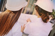 © Evgeniy Kalinovskiy - Two young pretty business women industrial engineers in construction helmets with a tablet in hands on a glass building background