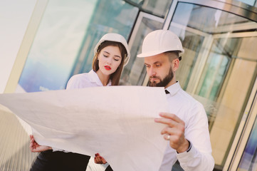 A man with a beard and a woman in business clothes is studying drawings and documents for a new project