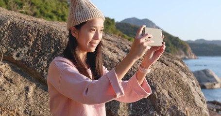 Poster - Woman taking photo on cellphone in seaside at sunset