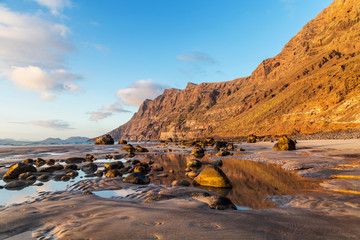 Wall Mural - Rocks and cliffs on the sandy beach of Caleta de Famara, famous surfing and kite surfing resort on Lanzarote, Canary Islands, Spain