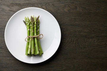 Wall Mural - Bunch of fresh asparagus in white plate on dark wooden background, top view