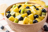 Fototapeta Mapy - Fresh fruit salad with pineapple, mango, kiwi and blueberries on white wooden background.