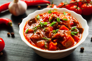 Goulash. Vegetable rague with eggplant, pepper, tomato and carrot in white bowl on dark wooden background