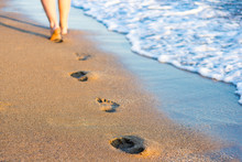 Summer, Travel And Vacation Concept - Legs, Footprints In The Sand And Sea Wave
