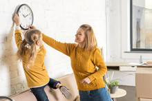 Happy Mother And Daughter Hanging Clock On Wall During Relocation