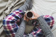 Girl sat on bed in cozy pyjamas drinking a cup of tea