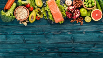 Wall Mural - Healthy food. Fish salmon, avocado, broccoli, fresh vegetables, nuts and fruits. On a wooden background. Top view. Copy space.