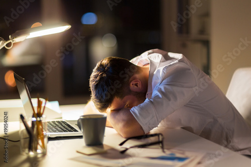 Fotografía tired businessman lying on table at night office
