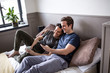 © ReeldealHD images - Young male couple sitting on bed and looking at smartphone together