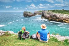 Father And Son Backpacker Travelers Rest On The Rocky Sea Side And Enjoy With Beautiful View