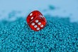 один красный игровой кубик в куче мелких синих камней