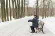 © YuSafa - Man - elderly pensioner, sits on a park bench in the winter. High trees, a lantern.