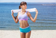A beautiful sports woman holds white towel in her hands  in the summer against the background of the sea coast.