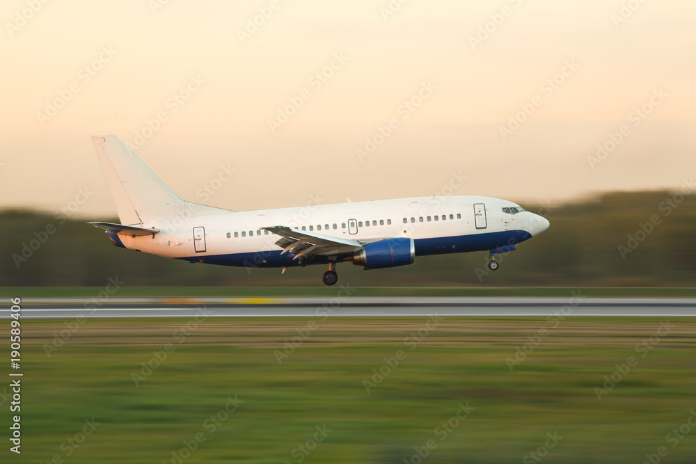 narrow-bodied passenger airplane landing at international airport during sunset, in motion, side view, copy space for text/ airplane climbs after take off/ Landing aircraft low over the runway - obrazy, fototapety, plakaty 