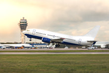 Airplane In Takeoff Mode, Side View/ Aircraft Flies Against The Backdrop Of Air Traffic Control Tower And Airplanes On The Platform/ The Plane Takes Off From The Airport Runway, Copy Space For Text
