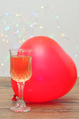 Wall Mural - A glass of champagne and heart shape balloon against an out of focus light background