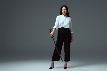 Wall Mural - full length view of beautiful young asian woman holding katana and looking at camera on grey