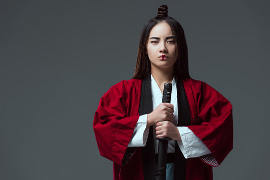 asian woman in kimono holding katana sword and looking at camera isolated on grey