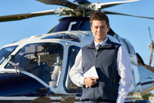 Portrait Of Pilot Standing In Front Of Helicopter With Digital Tablet