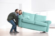 © Africa Studio - Young couple moving sofa in room at new home