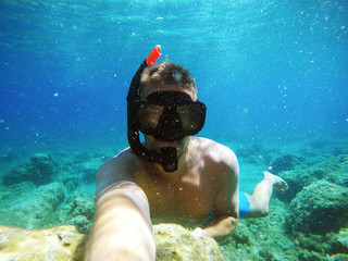 Wall Mural - Handsome young adventuristic scuba diver man taking a selfie with an action camera in the turquoise sea.