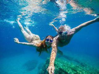 Wall Mural - Underwater selfie with a stick of young beautiful attractive joyful love couple exploring and enjoying with goggles in the exotic turquoise sea at summer holiday or honeymoon.