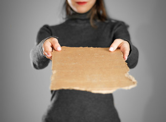 Wall Mural - A young girl in a grey jacket holding a piece of cardboard. Prepared for your text