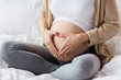 © Syda Productions - happy pregnant woman making heart gesture in bed