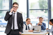 © LIGHTFIELD STUDIOS - Smiling businessman talking on smartphone in front of his colleagues in modern office
