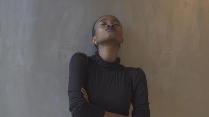 Portrait of the attractive isolated african girl leaning on the gray wall with closed eyes and arms crossed.