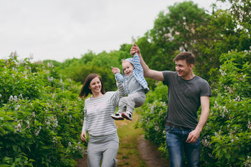 Man, woman walking on nature bush background holding hands little cute child baby boy. Mother, father, little kid son play, have fun. Parenthood, family day 15 of may, love, parents, children concept.