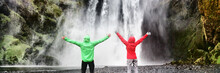 Adventure Travel In Amazing Nature Landscape. Couple Tourists Enjoying Freedom On Vacation At Waterfall Banner Panorama . People With Open Arms In Success, Summer Holiday In Iceland.