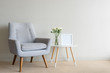 Retro armchair and small round table with roses in glass vase and blank square frame against beige wall