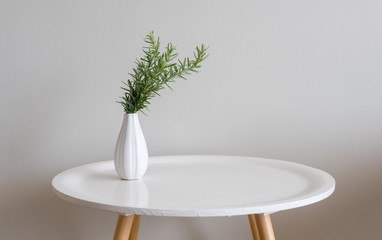 sprigs of rosemary in small white vase on round table against beige wall