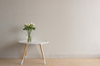 © Natalie Board - White roses in glass vase  on small round table against beige wall
