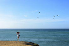 Girl On The Distance  Taking Photos Of Pelicans Flying Over Sea