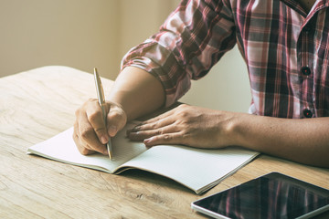 Close up view hands of person writing idea to notebook in blank pages on the wooden table beside the window and have sunlight from window.