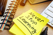 Never stop learning written on a memo stick. Lifelong learning concept.