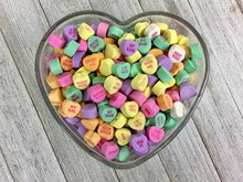 Valentine's Day Candy Hearts In A Heart Shaped Glass Dish On A Distressed Wood Surface
