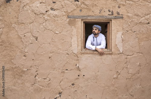 arab man in traditional omani outfit in an old castle, looking out of a window Poster Mural XXL