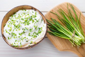 Bowl of cream cheese with green onions, dip sauce on wooden table.