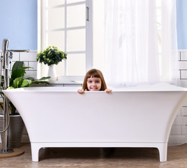 Wall Mural -  Happy little baby girl sitting in bath tub playing with duck toys  in the bathroom