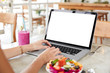 © WHstudio Leushin N - Successful female freelnacer uses laptop with blank screen during vacations in exotic country, does remote job, surrounded with fresh smoothie and fruit salad, enjoys free internet connection in cafe.