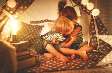 Wall Mural - happy family children brother and sister play, laugh and hug   in dark tent in playroom