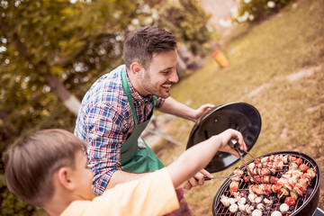 Wall Mural - Father and son having a barbecue party in their garden in summer.