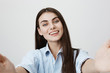 © Cookie Studio - Pretty and slim caucasian woman smiling happily while stretching hands towards camera as if holding it, standing over gray background. Girl speaks with her mother via tablet while walking