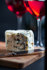 Roquefort cheese on a wooden board. and two glasses of red wine